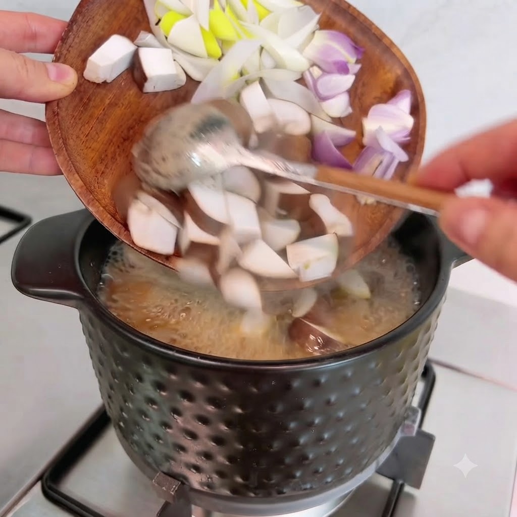 Setas shiitake, cebollas y cebollinos en cubitos siendo vertidos desde un plato de madera en la olla.