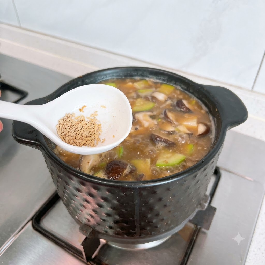 Una cuchara blanca sosteniendo caldo de res en polvo posicionado sobre una olla burbujeante de Doenjang Jjigae.
