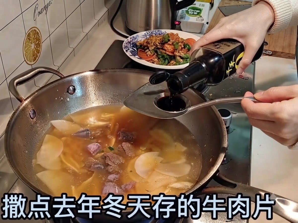 Salsa de soja vertiéndose en un caldo a fuego lento que contiene tiras de ternera y verduras.