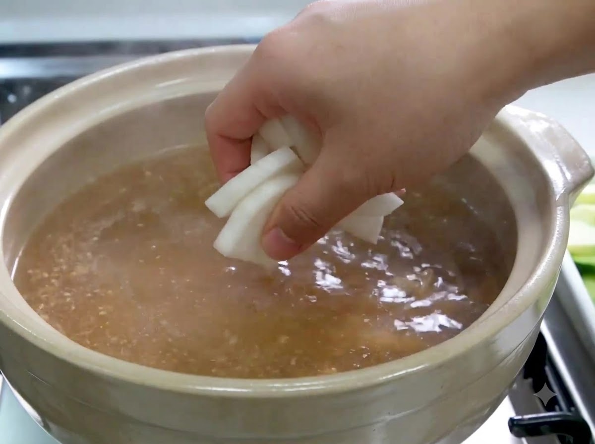 Una mano colocando rodajas de rábano blanco en una olla de caldo a fuego lento.
