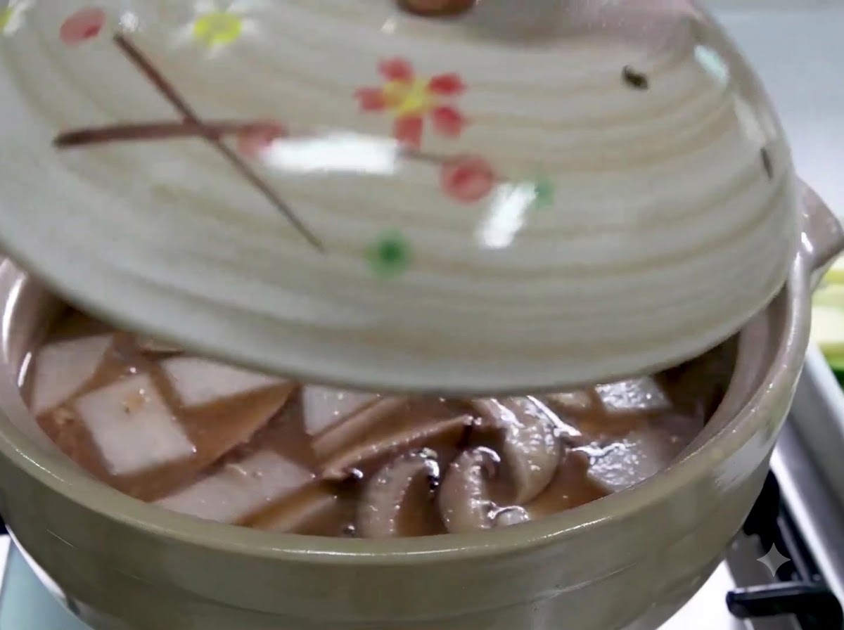 Una mano colocando una tapa en una olla de cerámica llena de caldo, rábano en rodajas y setas shiitake.