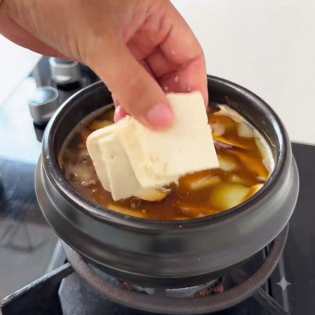Trozo de tofu añadido a la sopa que contiene rodajas de calabacín y setas enoki.