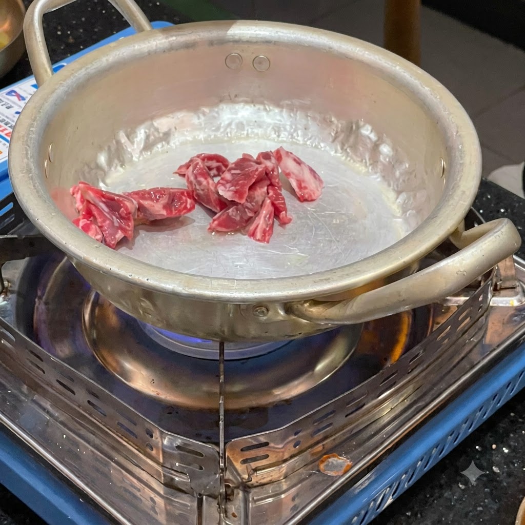 Trozos de ternera cruda siendo salteados en una pequeña olla de metal sobre un quemador de gas portátil encendido.