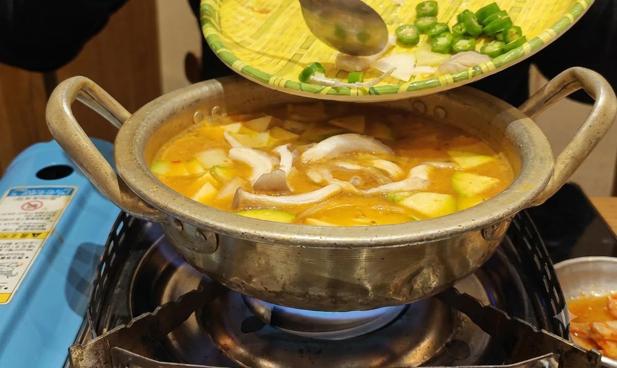 Verduras preparadas deslizándose desde una bandeja de mimbre hacia la olla hirviendo del estofado.