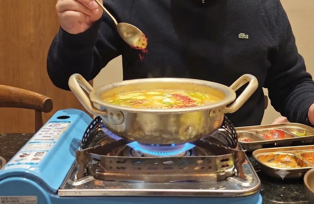 Una cucharada de chile en polvo rojo siendo espolvoreada sobre una olla burbujeante llena de verduras y caldo.