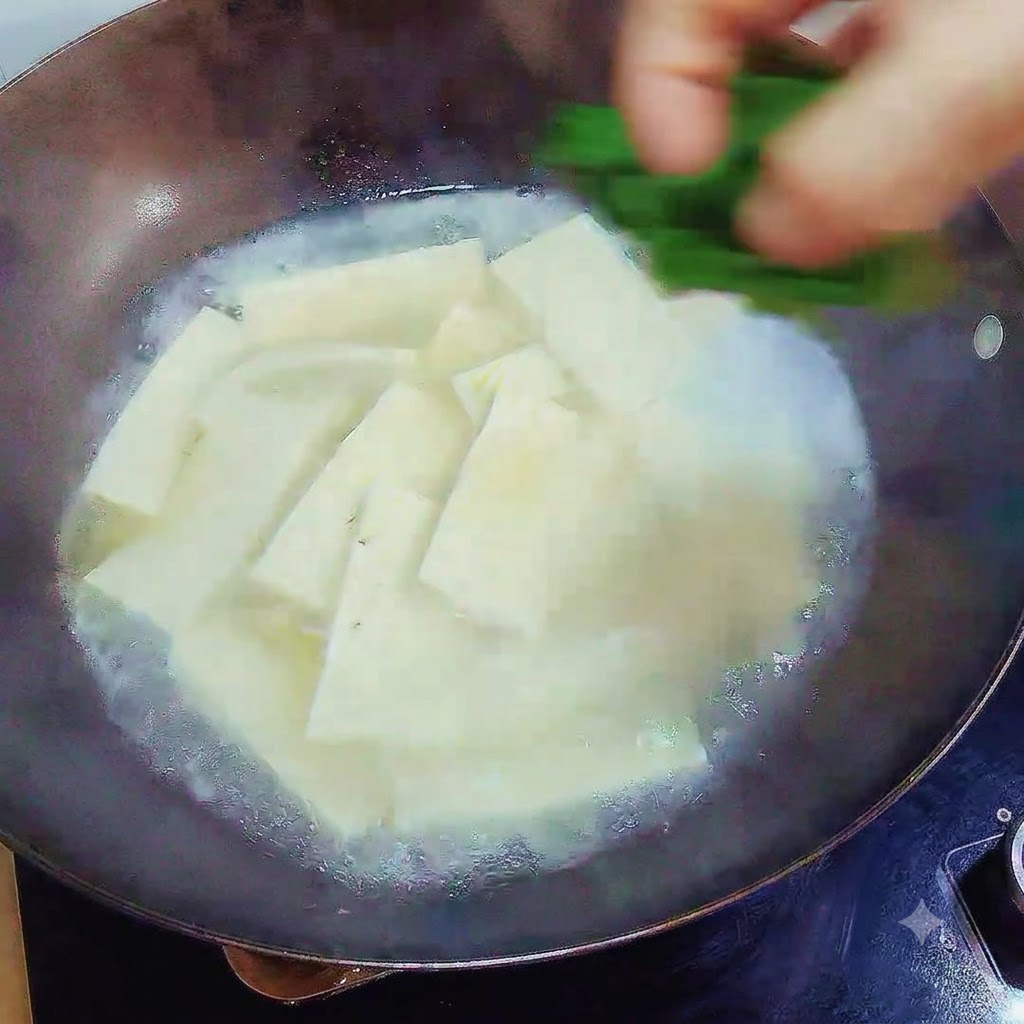 Una mano dejando caer cebollino verde picado sobre la sopa de tofu terminada en el wok.