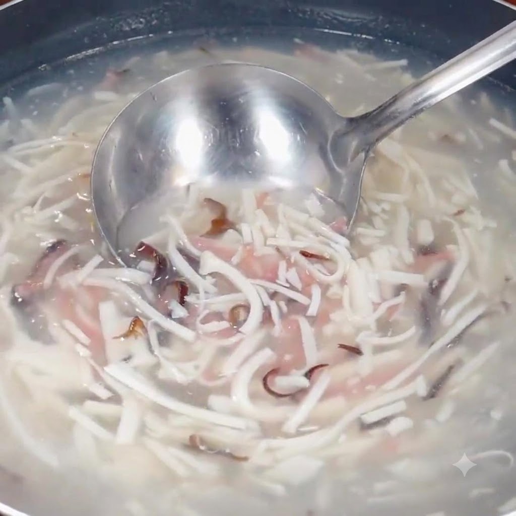 Un cucharón sacando la mezcla de sopa a fuego lento que contiene ingredientes en tiras en una olla.