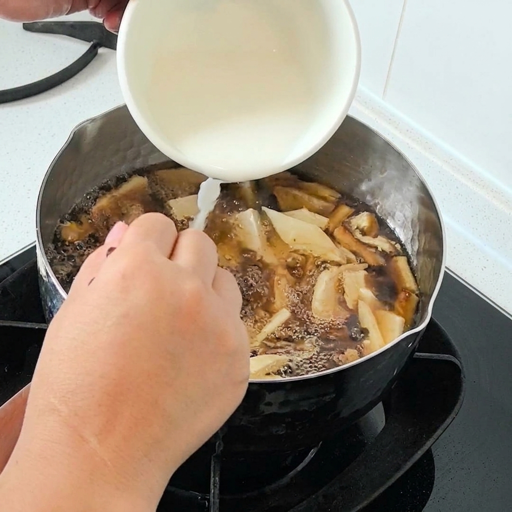 Almidón de agua siendo vertido desde un tazón blanco en una olla de sopa burbujeante.