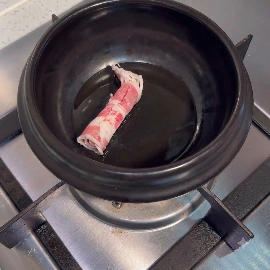 Tiras de carne cruda en una olla de cerámica oscura con aceite sobre el quemador de la estufa.