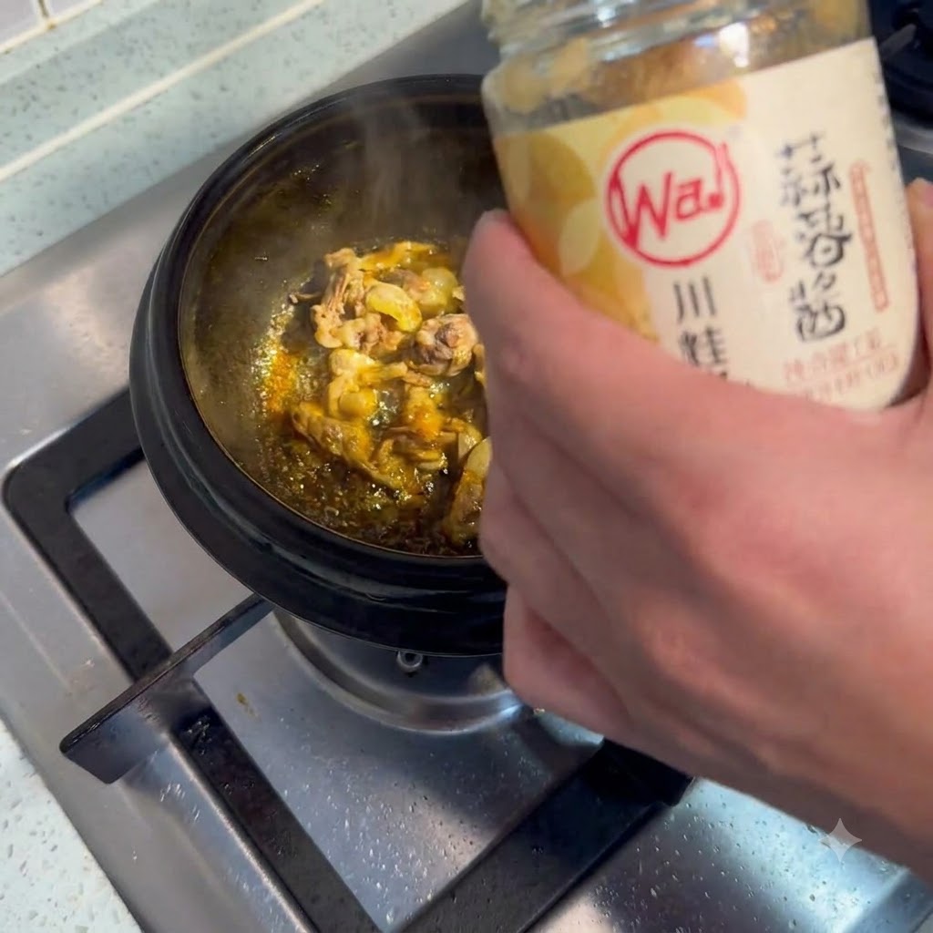 Una cucharada de pasta de ajo siendo agregada a una olla chisporroteante con carne.