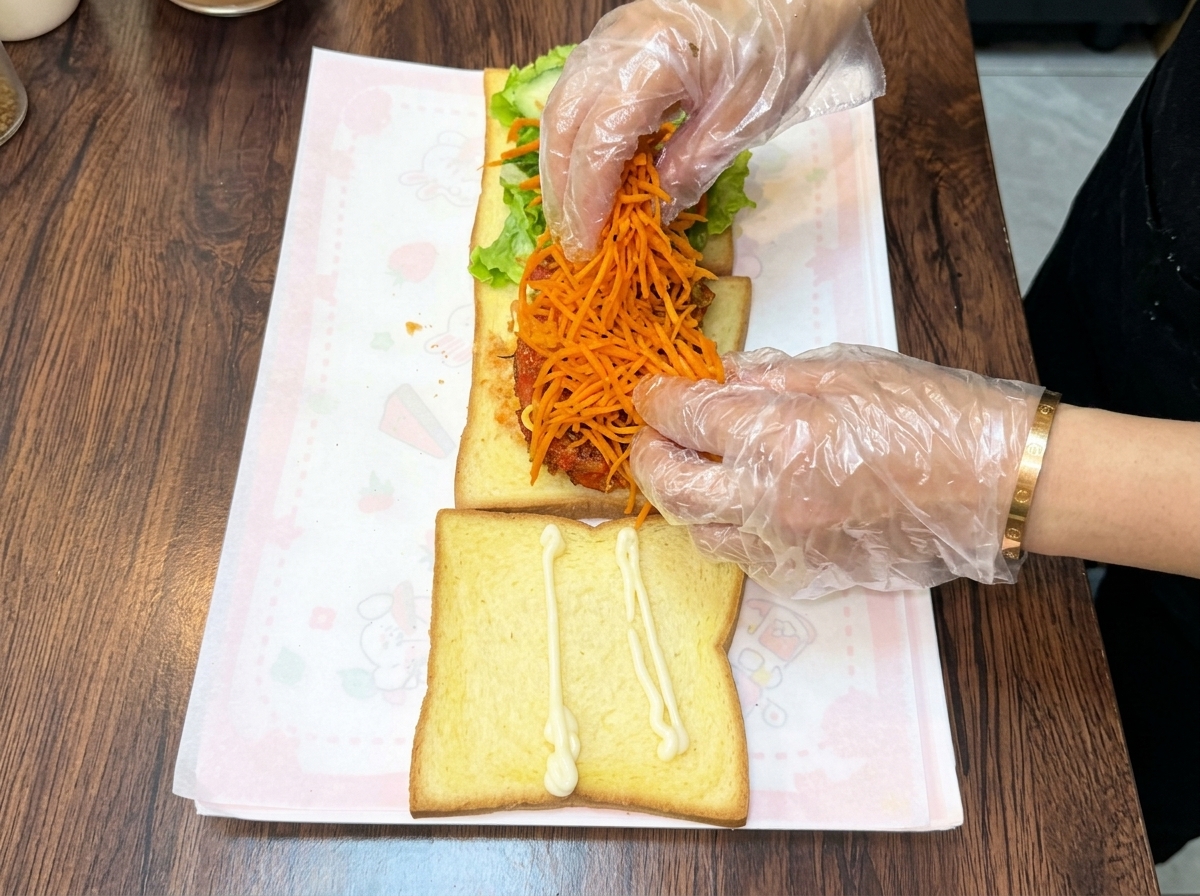 Manos con guantes amontonando un generoso montículo de zanahorias ralladas salteadas de color naranja brillante sobre la milanesa de pollo apilada.