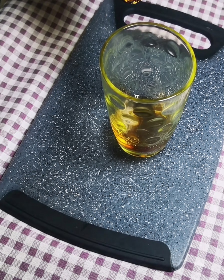 Salsa de soja oscura siendo vertida en un recipiente de vidrio transparente sobre una tabla de cortar gris.