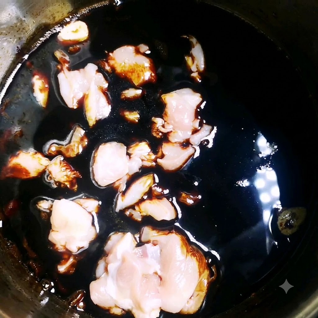 Trozos de pollo crudo cociéndose a fuego lento en una salsa oscura y sabrosa dentro de una olla.