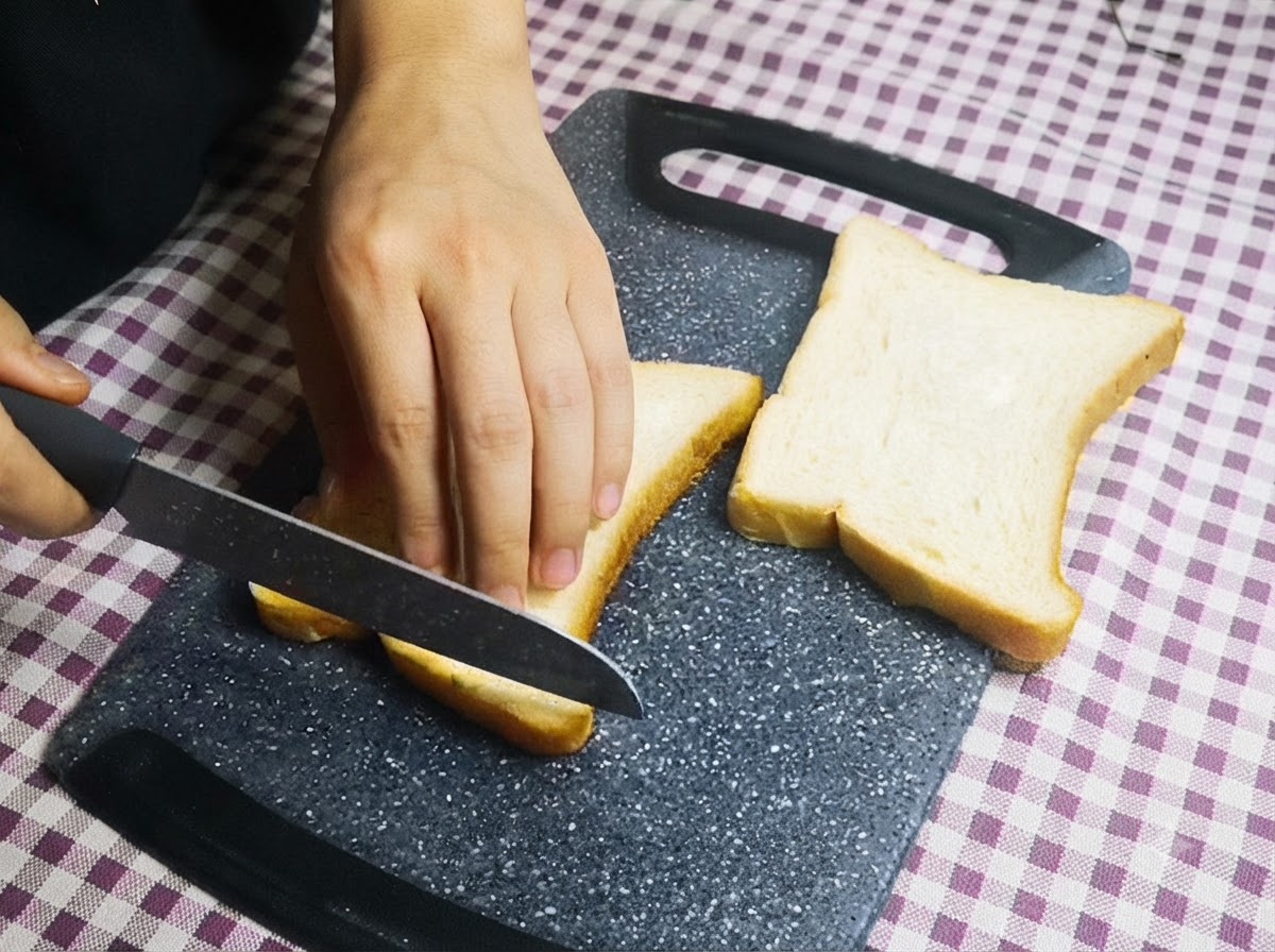 Una persona usando un cuchillo para quitar los bordes de rebanadas de pan blanco en una tabla de cortar.