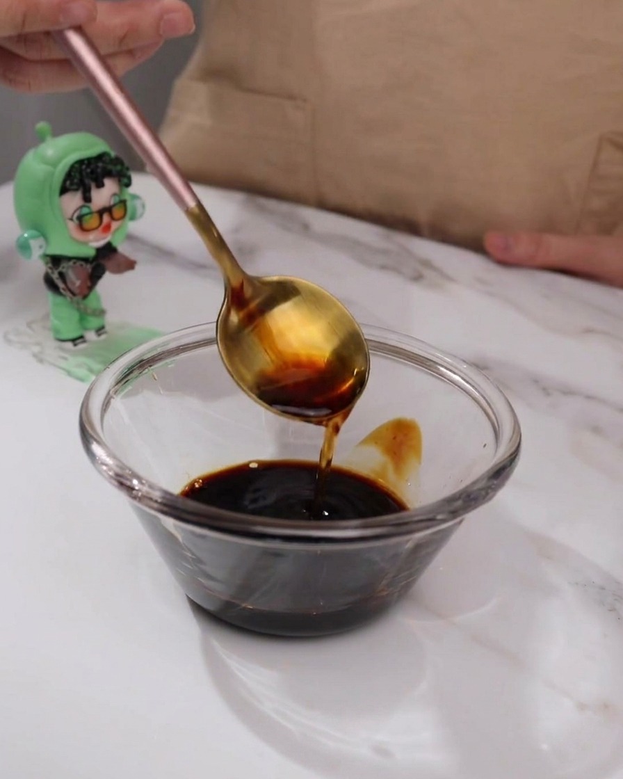 Ingredientes de la salsa teriyaki mezclándose en un pequeño bol de vidrio con una cuchara.