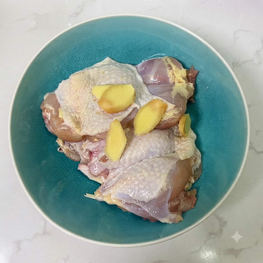Muslos de pollo y rodajas de jengibre dentro de un bol de cerámica azul con salsa de soja.