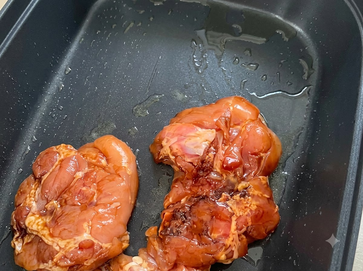 Trozos de pollo marinado colocados con la piel hacia abajo en una sartén antiadherente negra engrasada.