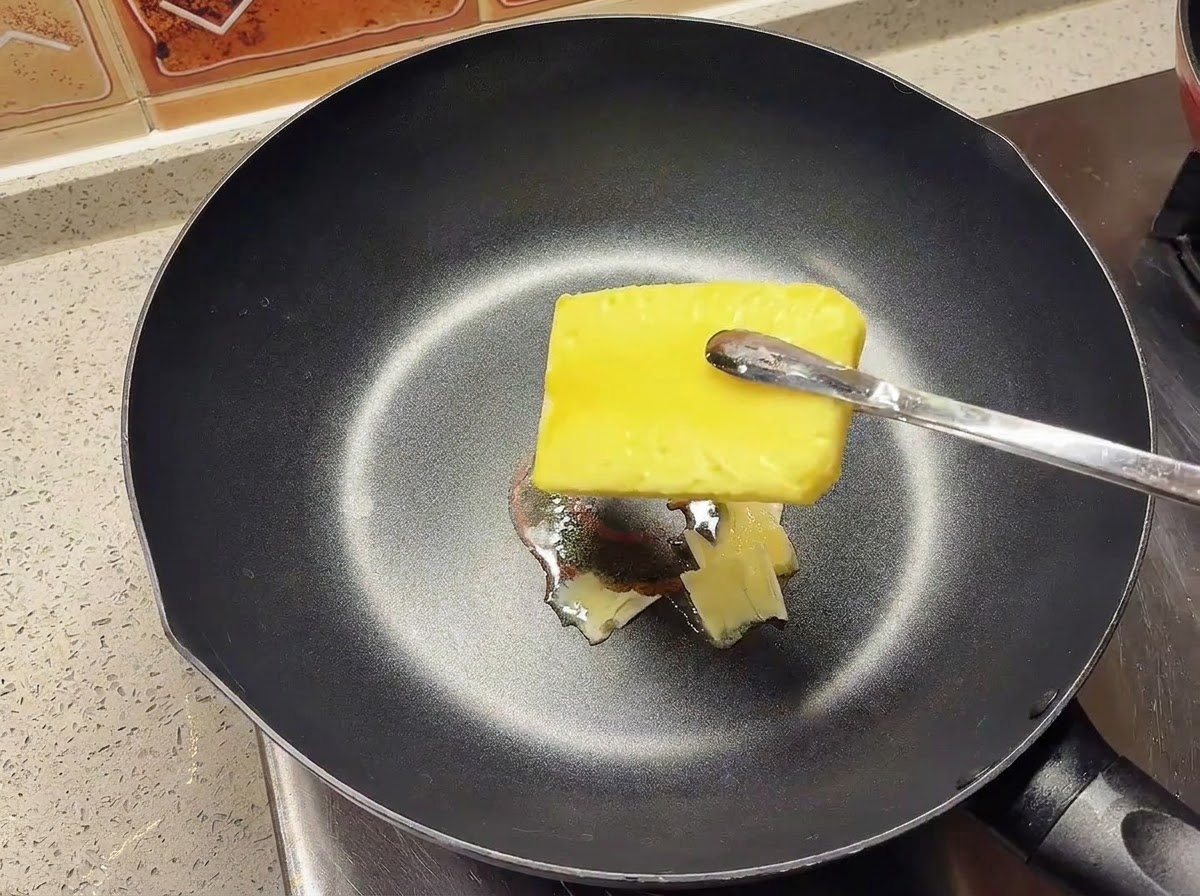 Un bloque de mantequilla amarilla derritiéndose en una sartén negra caliente.
