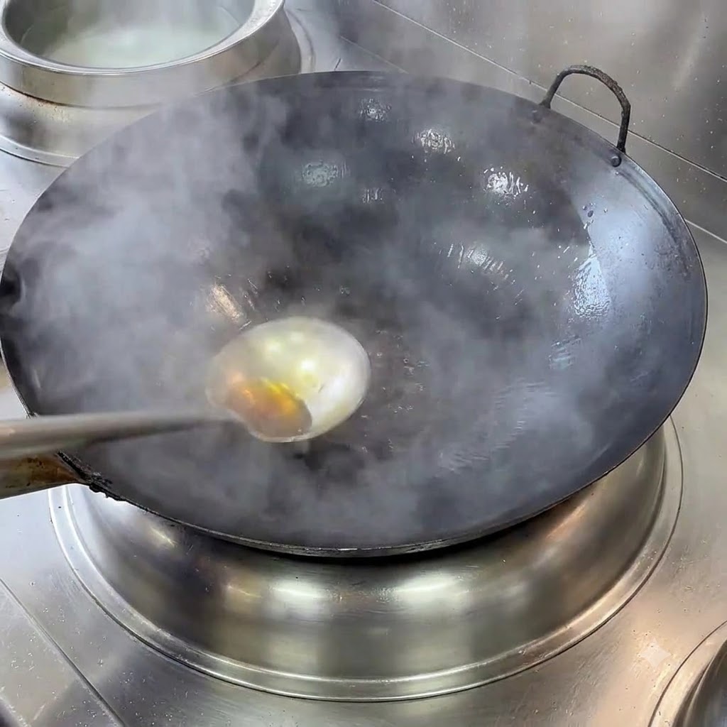 Un wok de hierro fundido humeante con un cucharón y aceite caliente calentándose en una estufa.