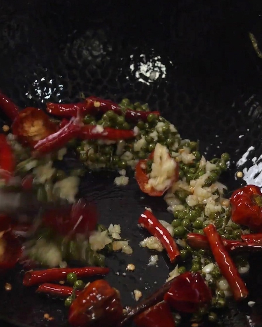 Costillas de cerdo fritas y aromáticos mezclándose juntos dentro de un wok.