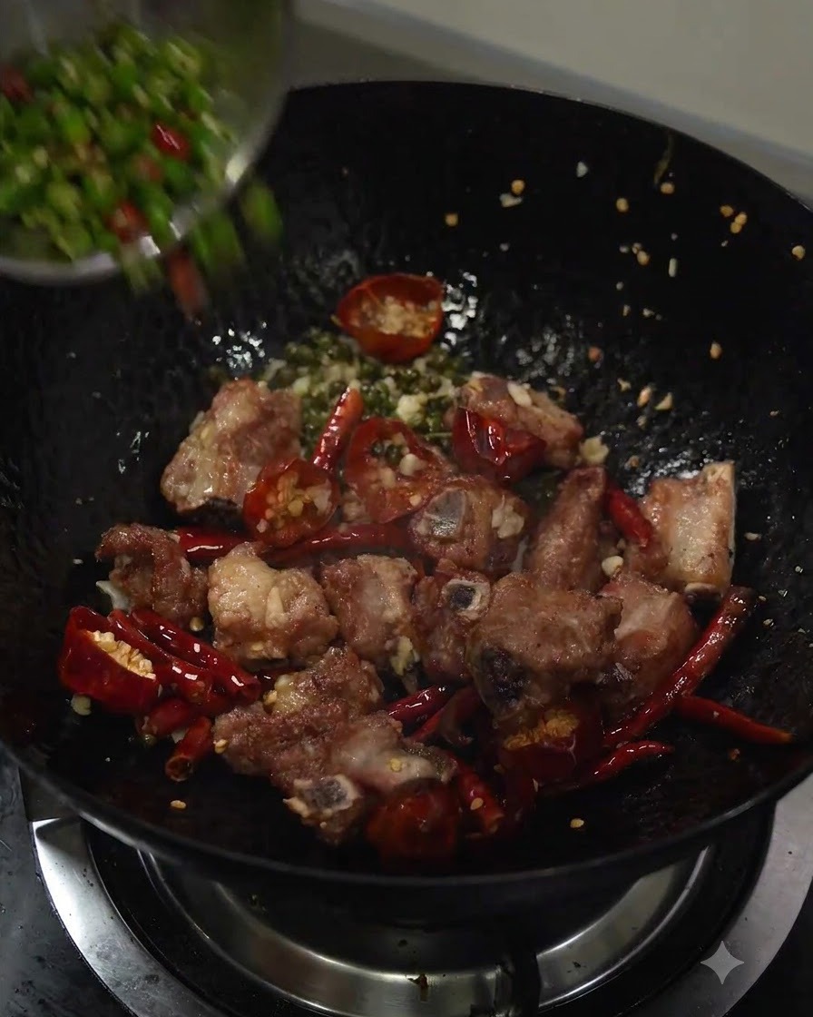 Chiles verdes cortados vertiéndose en el wok con las costillas de cerdo salteadas y los aromáticos.