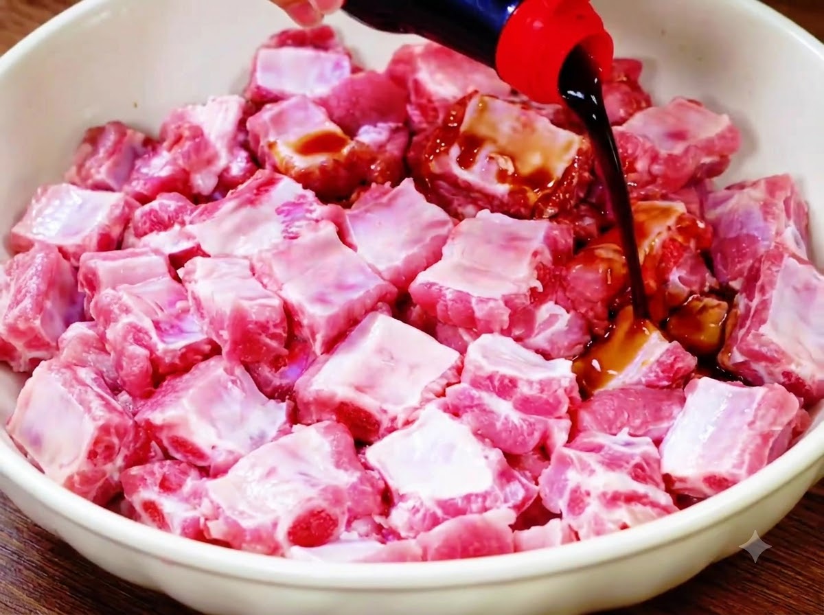 Salsa de soja ligera siendo vertida desde una botella sobre las costillas de cerdo crudas en un bol blanco.