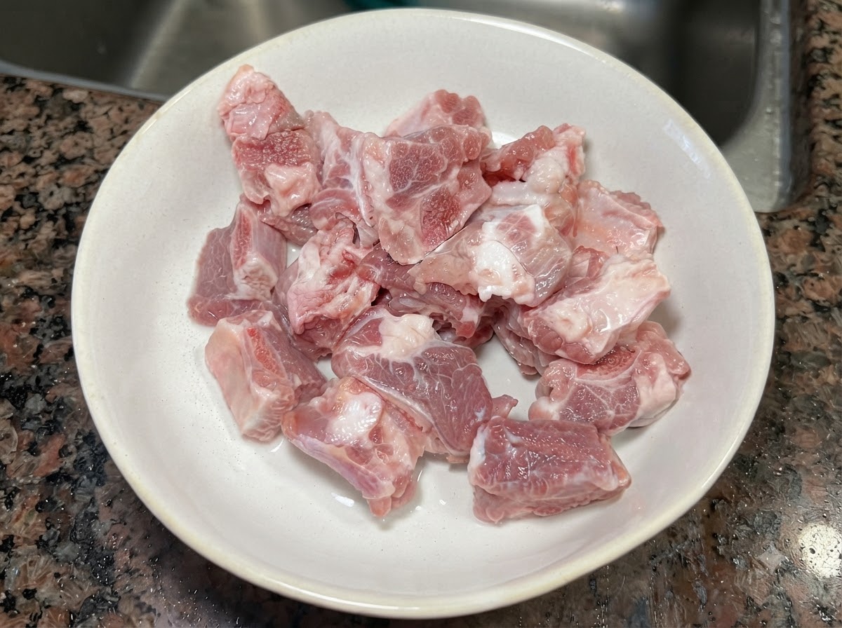 Trozos de costillas de cerdo crudas y frescas dentro de un bol de cerámica blanca.