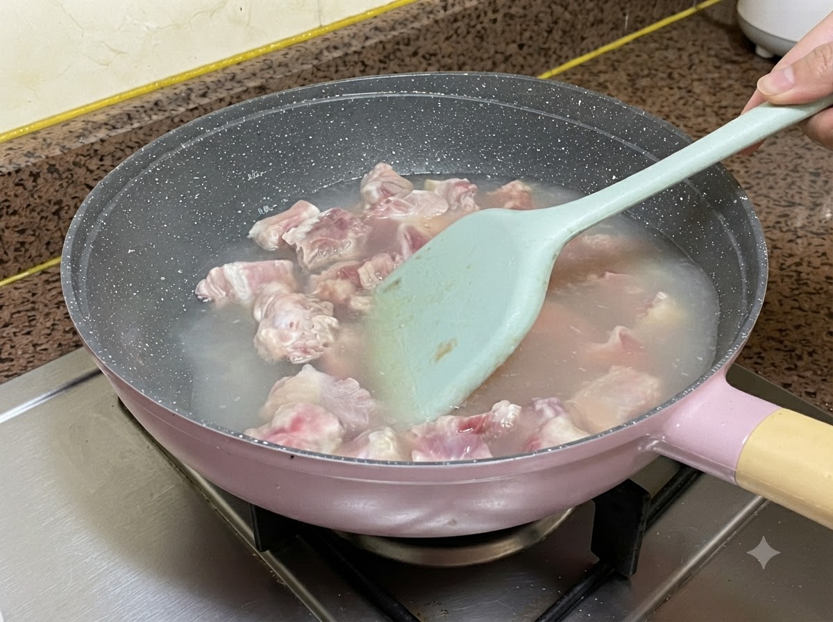 Costillas de cerdo hirviendo en agua dentro de una sartén mientras se remueven con una espátula de silicona azul claro.