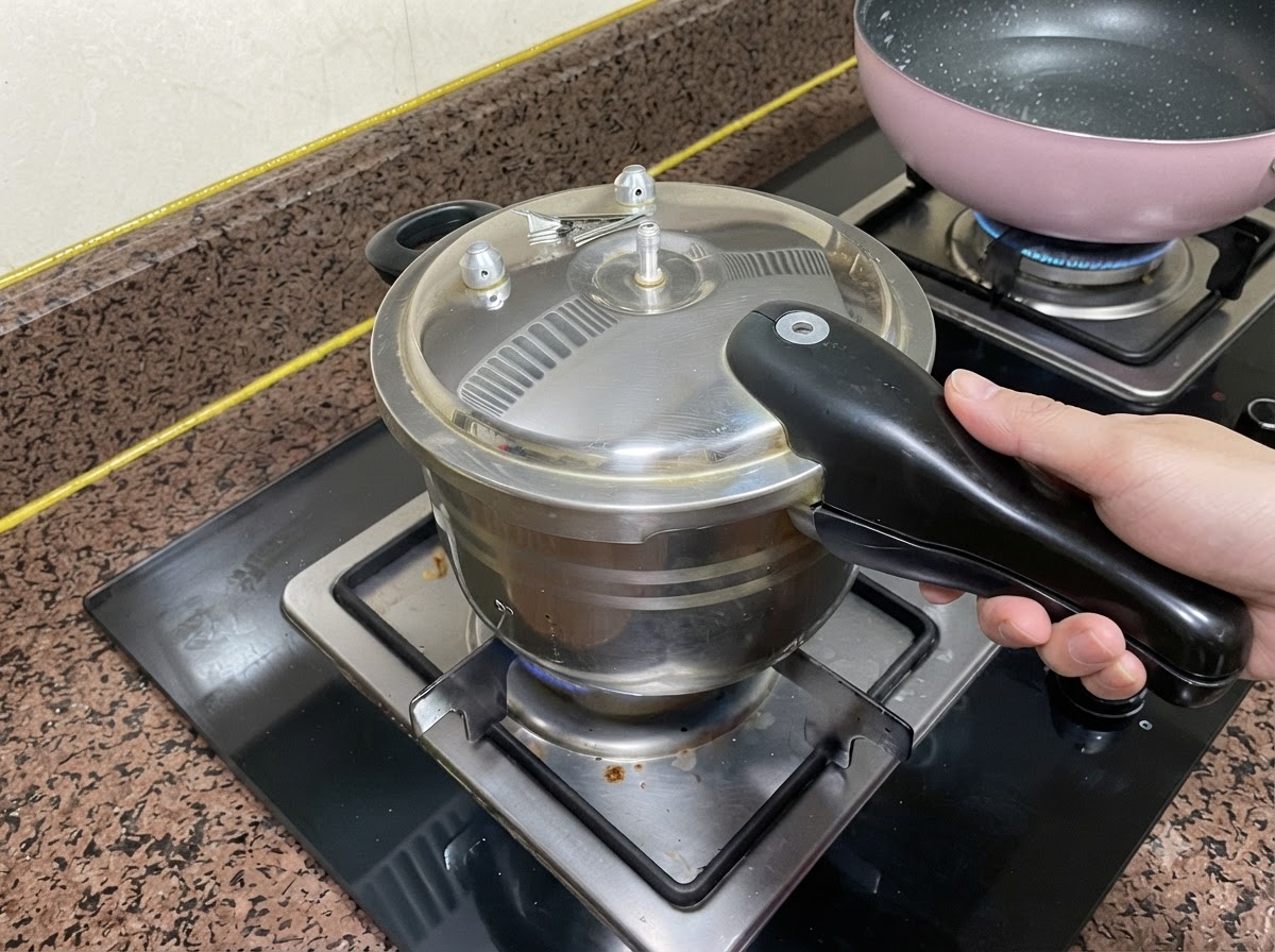 Tapa de una olla a presión cerrada en el quemador de la estufa con una mano agarrando el asa.