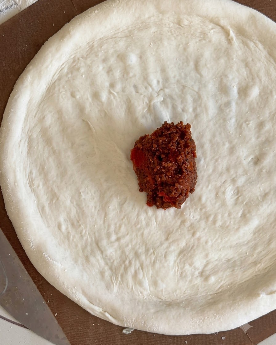Un pequeño montículo de salsa de carne roja en el centro de un círculo plano de masa de pizza.