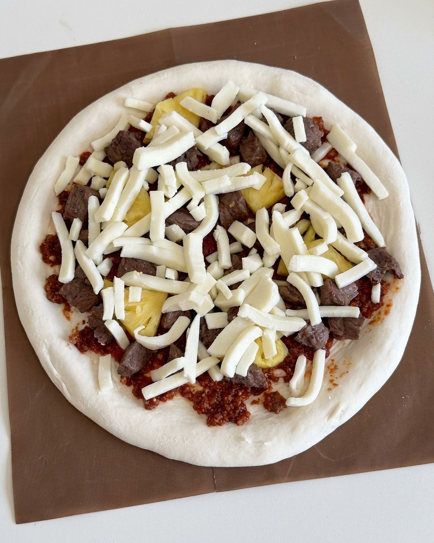 Queso blanco rallado esparcido generosamente sobre los ingredientes de ternera y piña de la pizza.