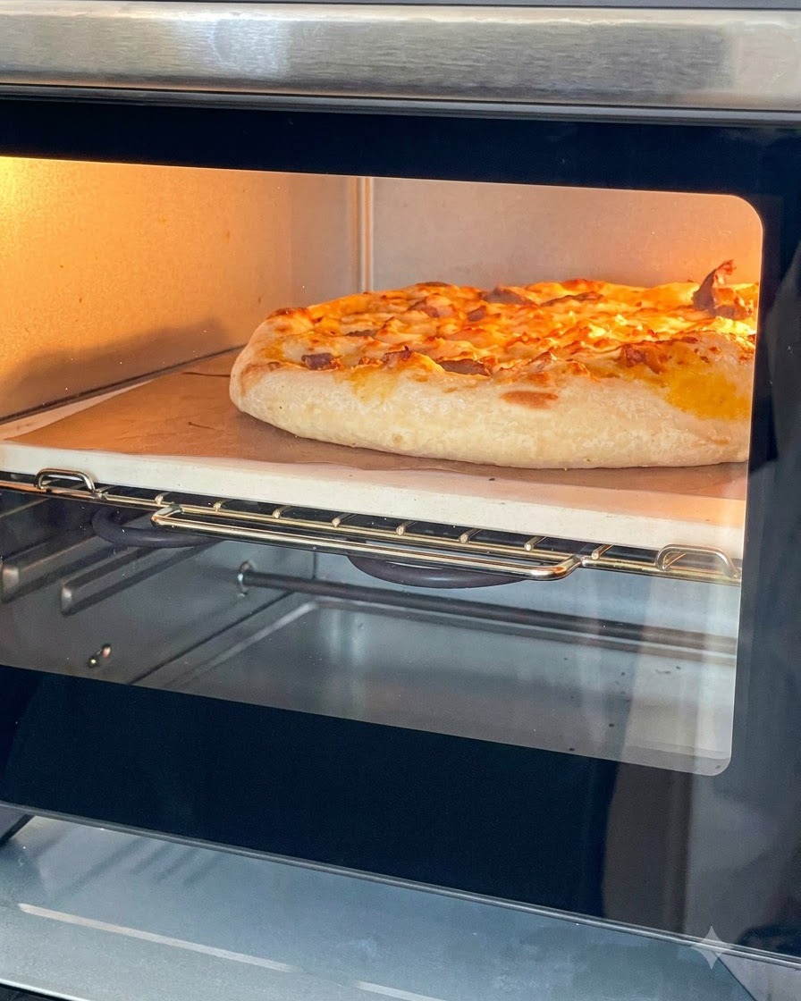 Una pizza dorada horneada con queso fundido dentro de un pequeño horno de sobremesa sobre una piedra de hornear.
