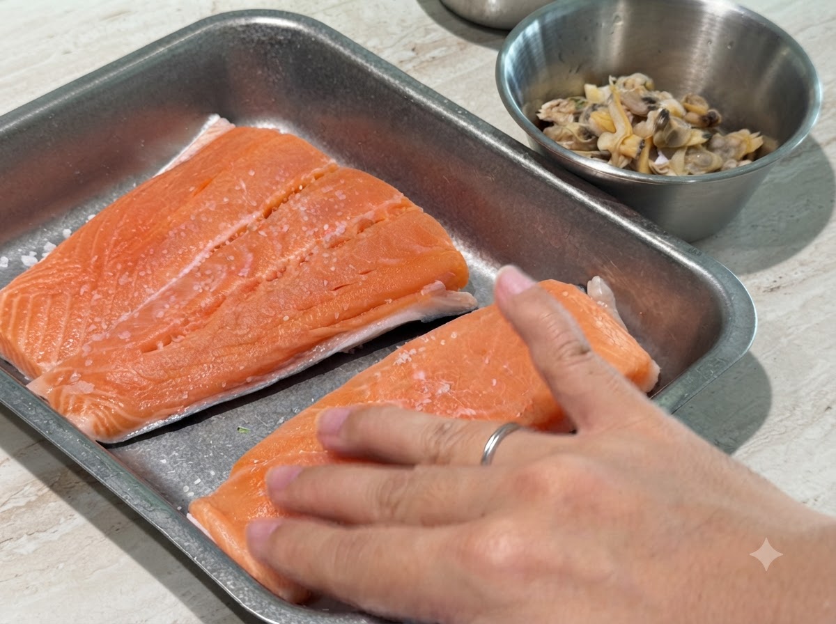 Una mano presionando ligeramente sal y pimienta negra sobre filetes de salmón crudo.