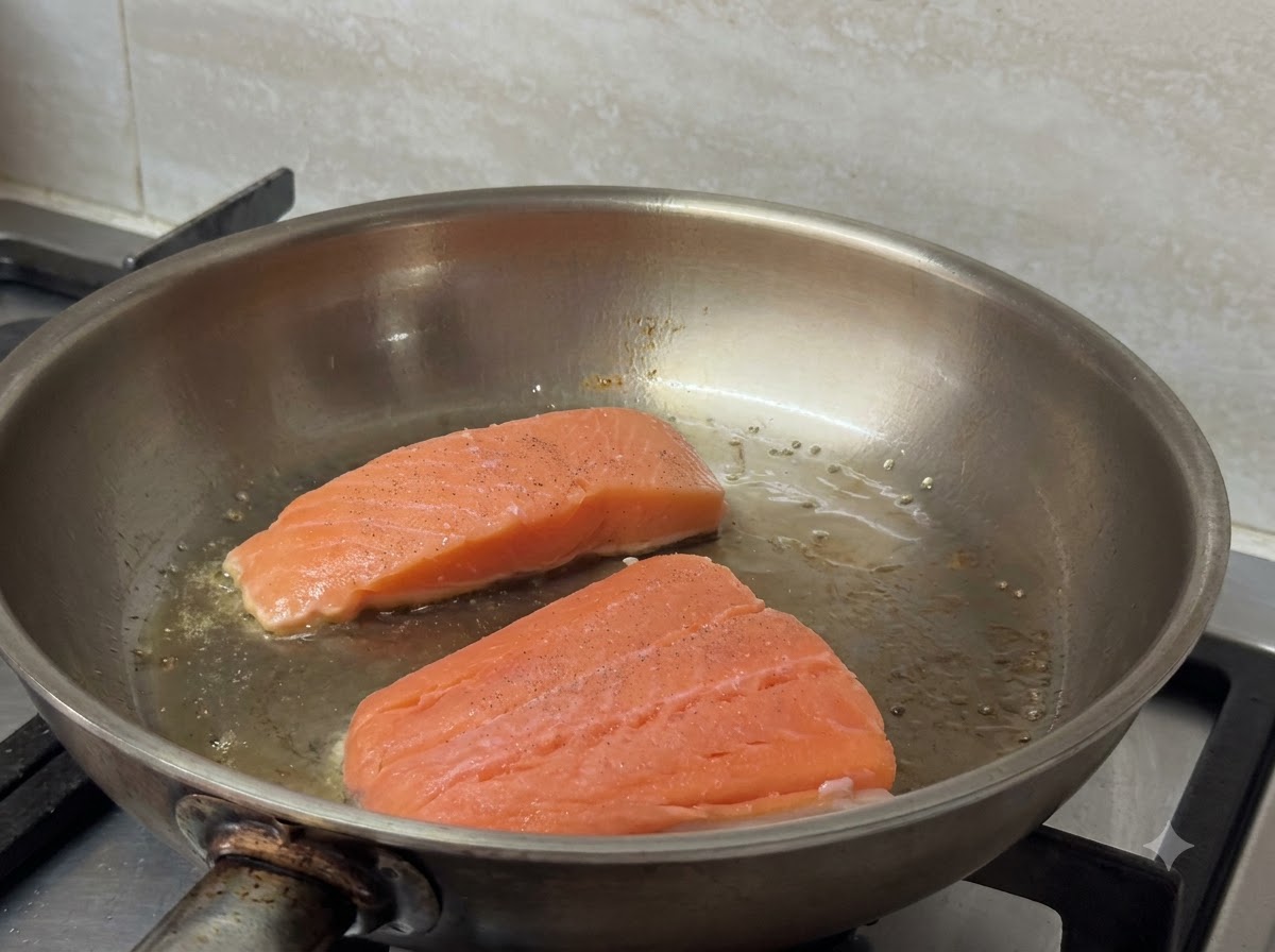 Dos filetes de salmón chisporroteando y dorándose en una sartén caliente.