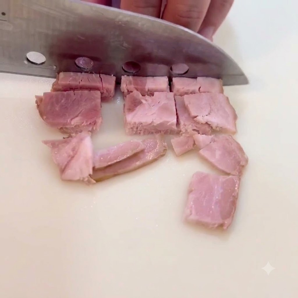 Rebanadas de tocino siendo cortadas en pequeños trozos cuadrados sobre una superficie de corte.