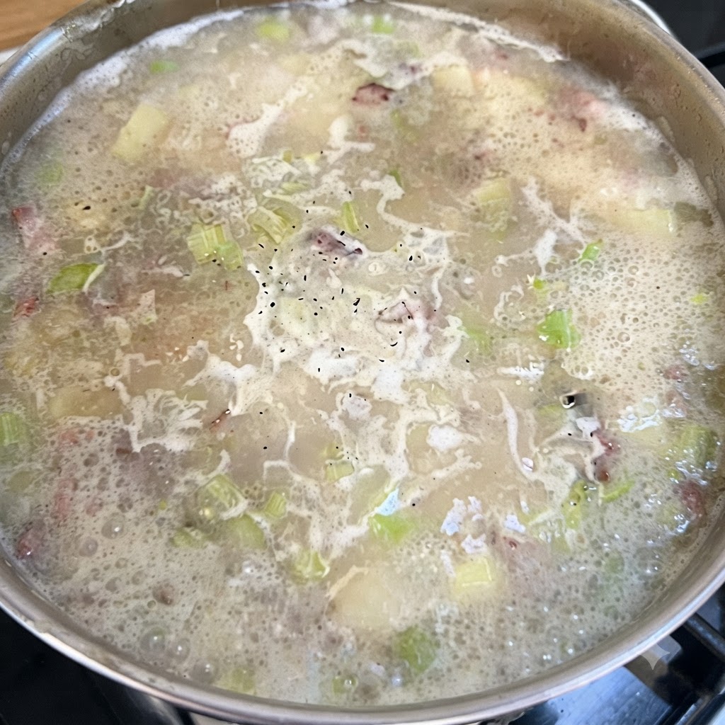 Una olla de base de sopa hirviendo a fuego lento con pimienta negra salpicada en la superficie burbujeante.