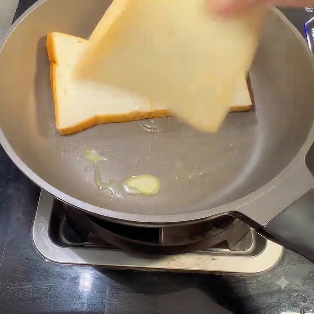 Tres rebanadas de pan de molde blanco colocándose dentro de una sartén con mantequilla.