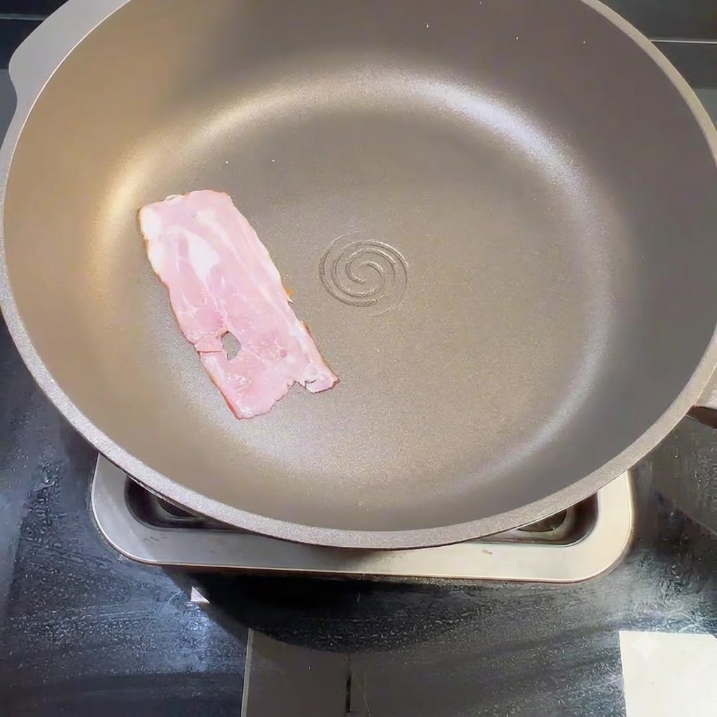 Una tira de tocino crudo colocada de forma plana dentro de una sartén seca en la estufa.