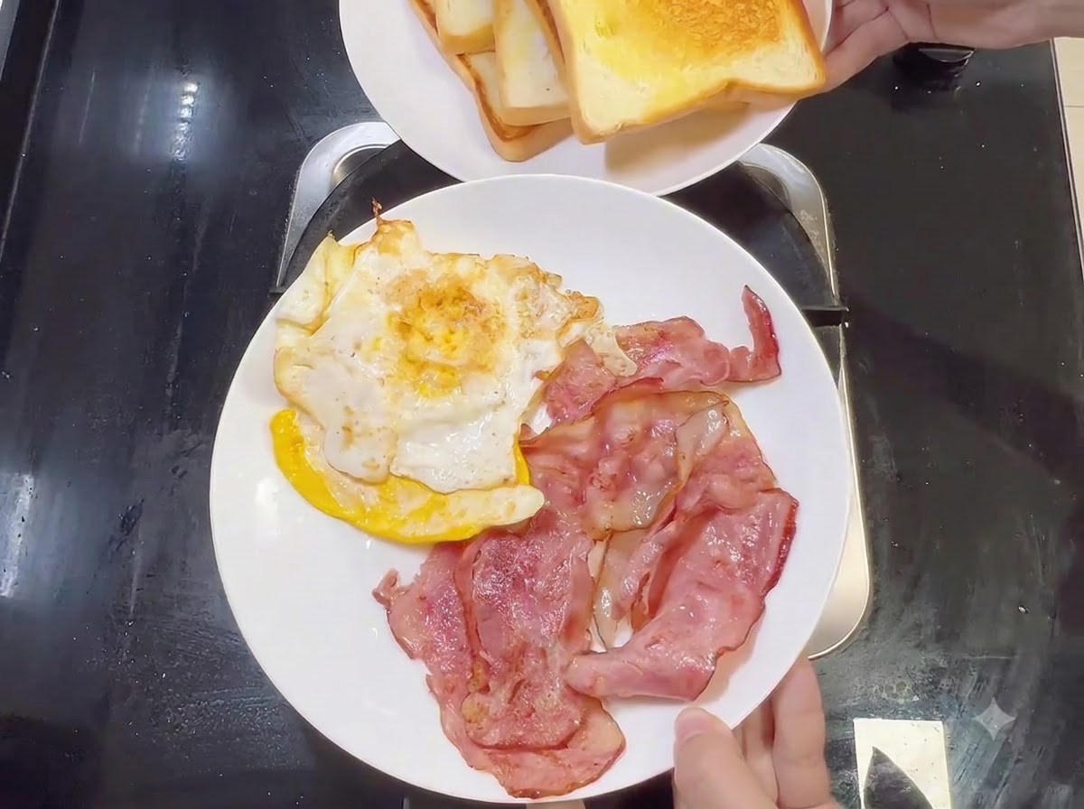 Un plato blanco con tiras de tocino cocido y huevos fritos, con otro plato de pan tostado sostenido arriba.