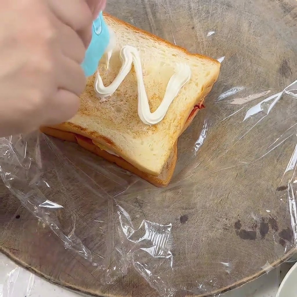 Expresando mayonesa en un patrón de zigzag sobre una rebanada de pan tostado.