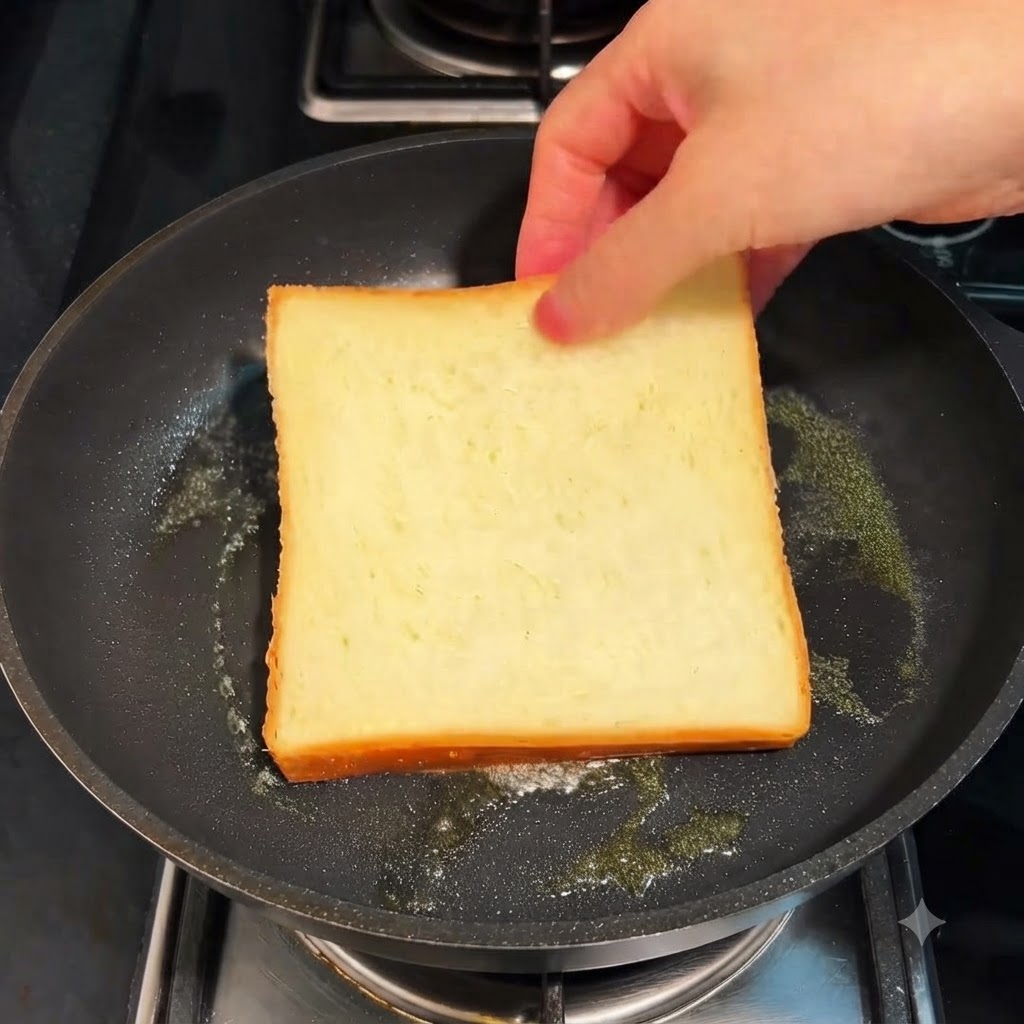 Una rebanada de pan blanco tostándose en una sartén con mantequilla a fuego lento.