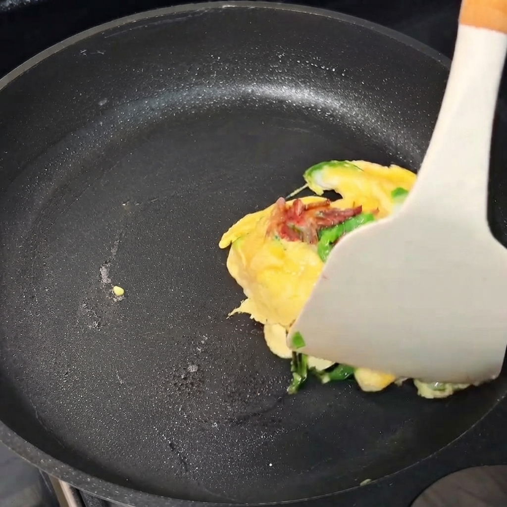 Un paquete de tortilla de huevo doblándose con una espátula dentro de una sartén.
