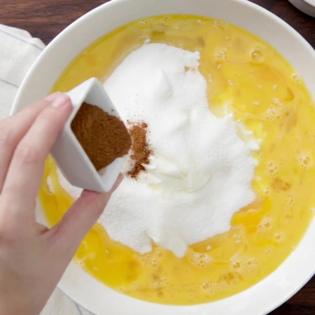 Polvo de canela siendo sacudido desde un plato pequeño cuadrado hacia la mezcla.