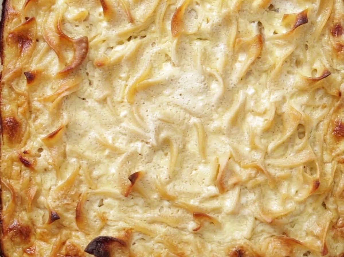 Un cuchillo cortando a través de un kugel horneado y refrigerado en un molde de vidrio para hornear.