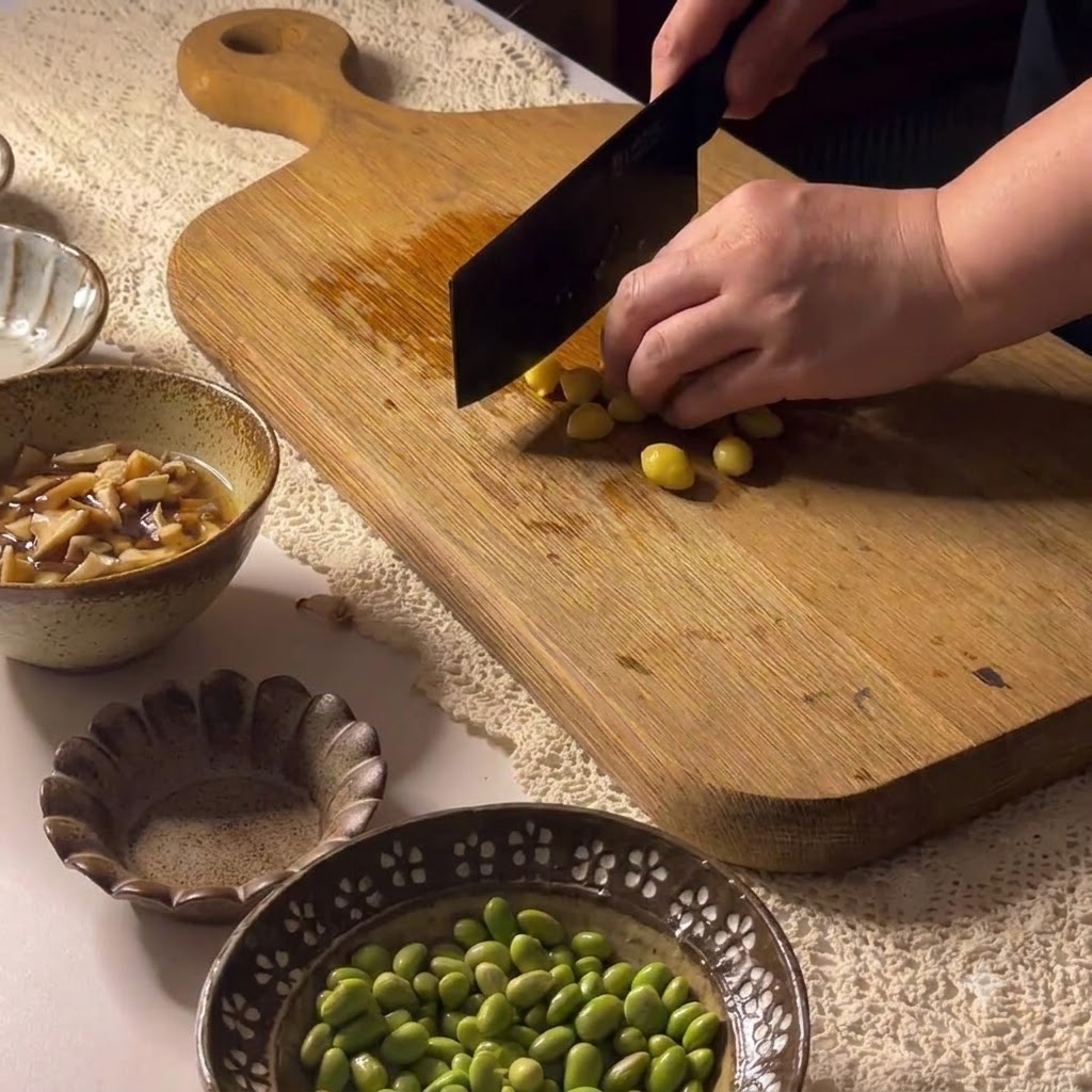 Nueces de ginkgo siendo cortadas en una tabla de cortar de madera con un cuchillo de carnicero.