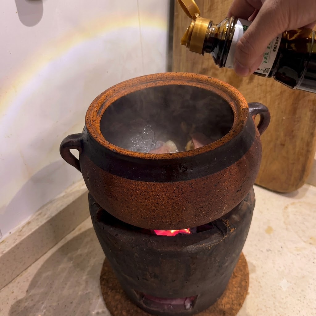 Salsa de soja siendo vertida desde una botella en una cazuela de barro situada sobre una estufa de carbón encendida.