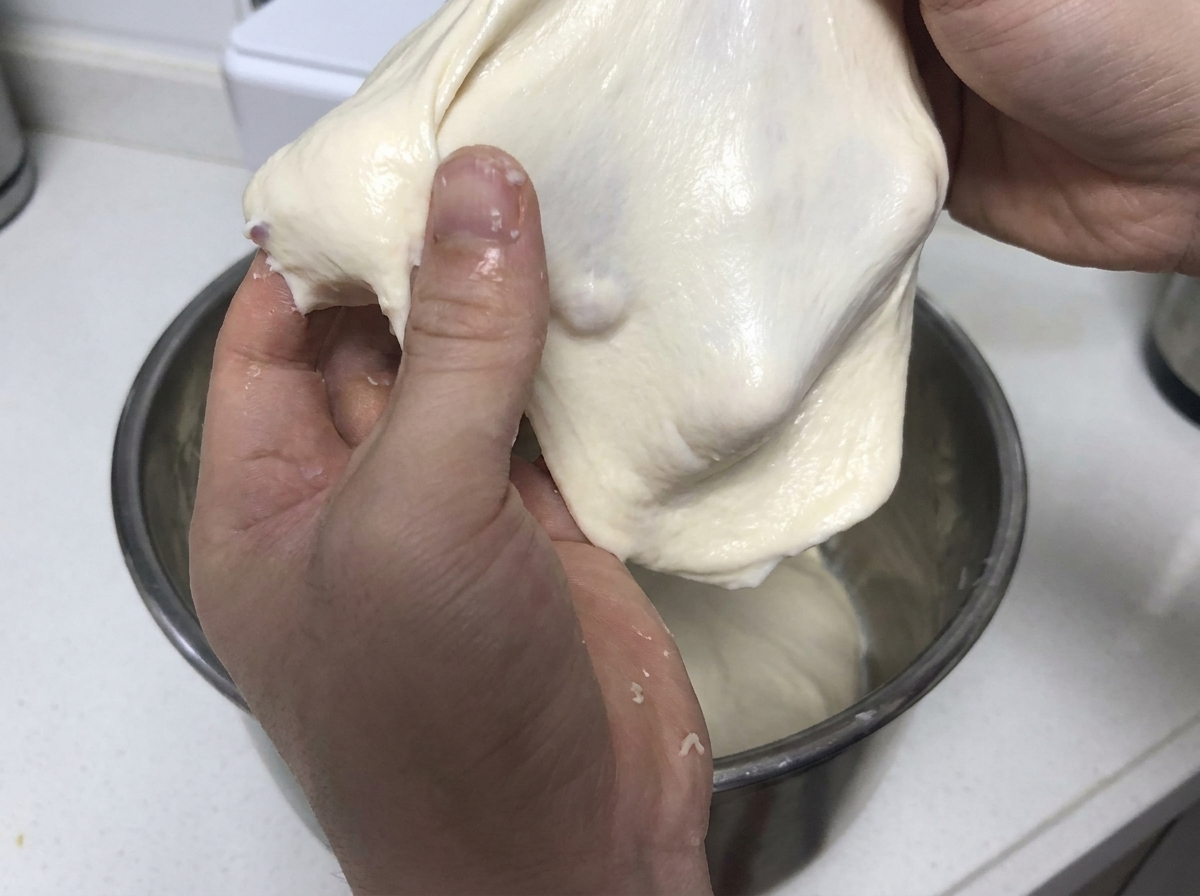 Manos tirando y estirando un trozo suave de masa blanca elástica para demostrar la fuerza del gluten.