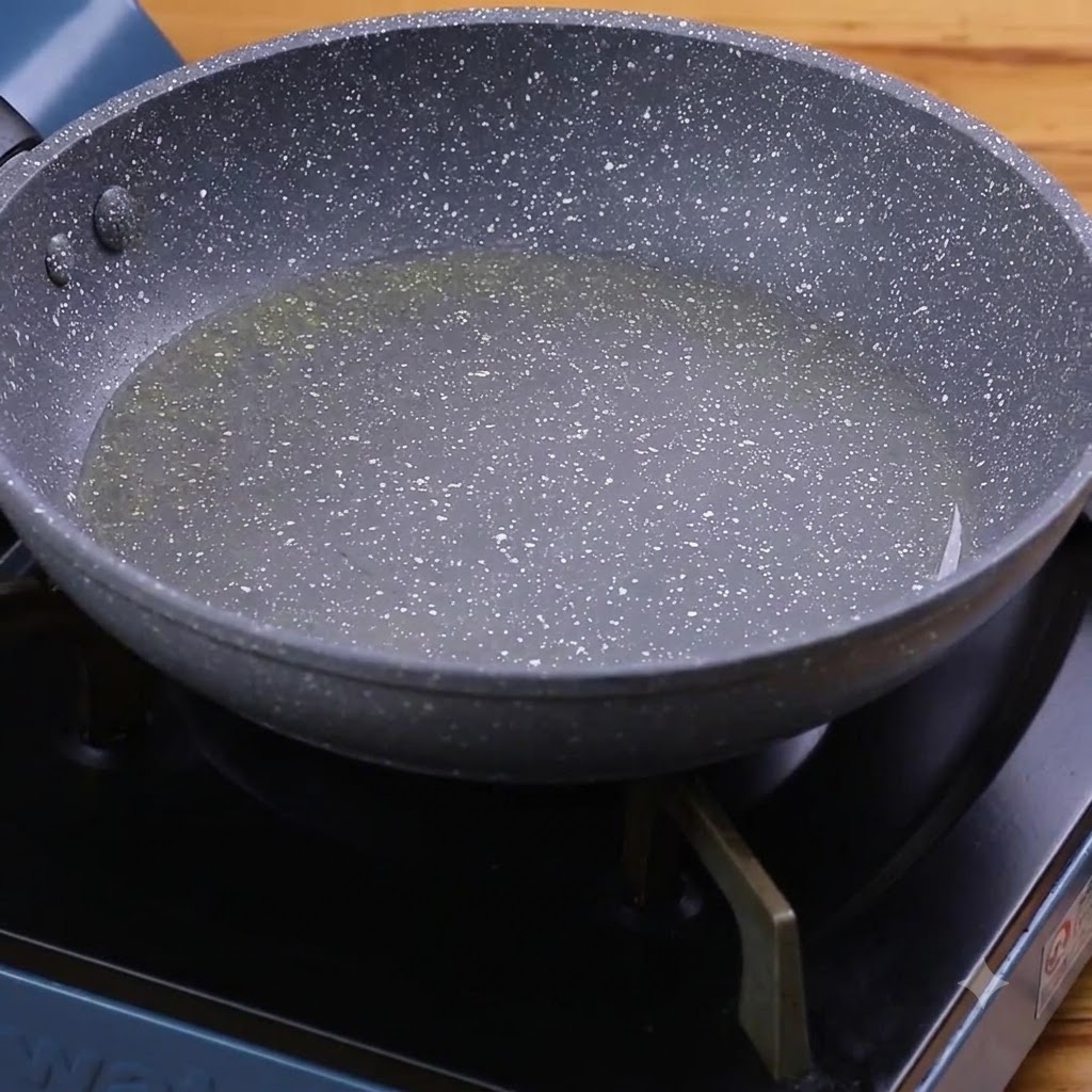 Ajo y pimientos verdes friéndose en aceite caliente dentro de una sartén moteada.