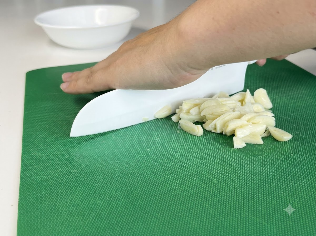 Dientes de ajo picándose finamente en una tabla de cortar con un cuchillo blanco.