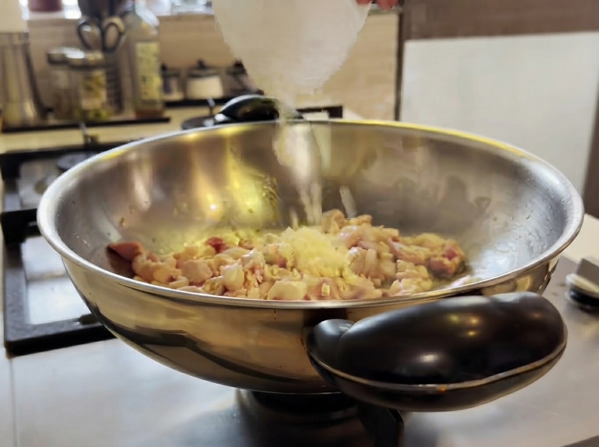 Ajo picado agregándose a un wok con pollo cocinándose y revolviéndose con una espátula.